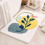 Tapis de salle de bain absorbant et épais, dans sa version jaune, au pied d'une baignoire, sur laquelle est déposée une serviette de bain.On aperçoit une paire de pantoufles à côté du tapis.