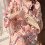 PHoto d'une femme assise avec un livre à la main portant un peignoir rose imprimé de pommes