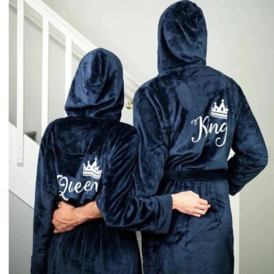 Photo d'un coupe de dos portant des peignoirs en peluche bleu à capuche avec inscrit Queen et King, debout devant un escalier