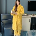 Femme portant un peignoir jaume et tenant un livre.