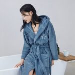 femme assise au bord d'une baignoire, de profil, portant un peignoir polaire de couleur bleu