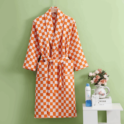 photo d'un peignoir en nid d'abeille a motif damier orange et blanc sur fond vert avec une petite table et des fleurs
