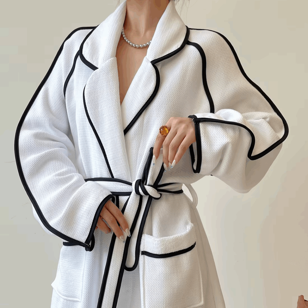 photo d'une femme portant un peignoir en nid d'abeille blanc avec des surpiqures noires qui le rendent très élégant. Elle noue la ceinture du peignoir.