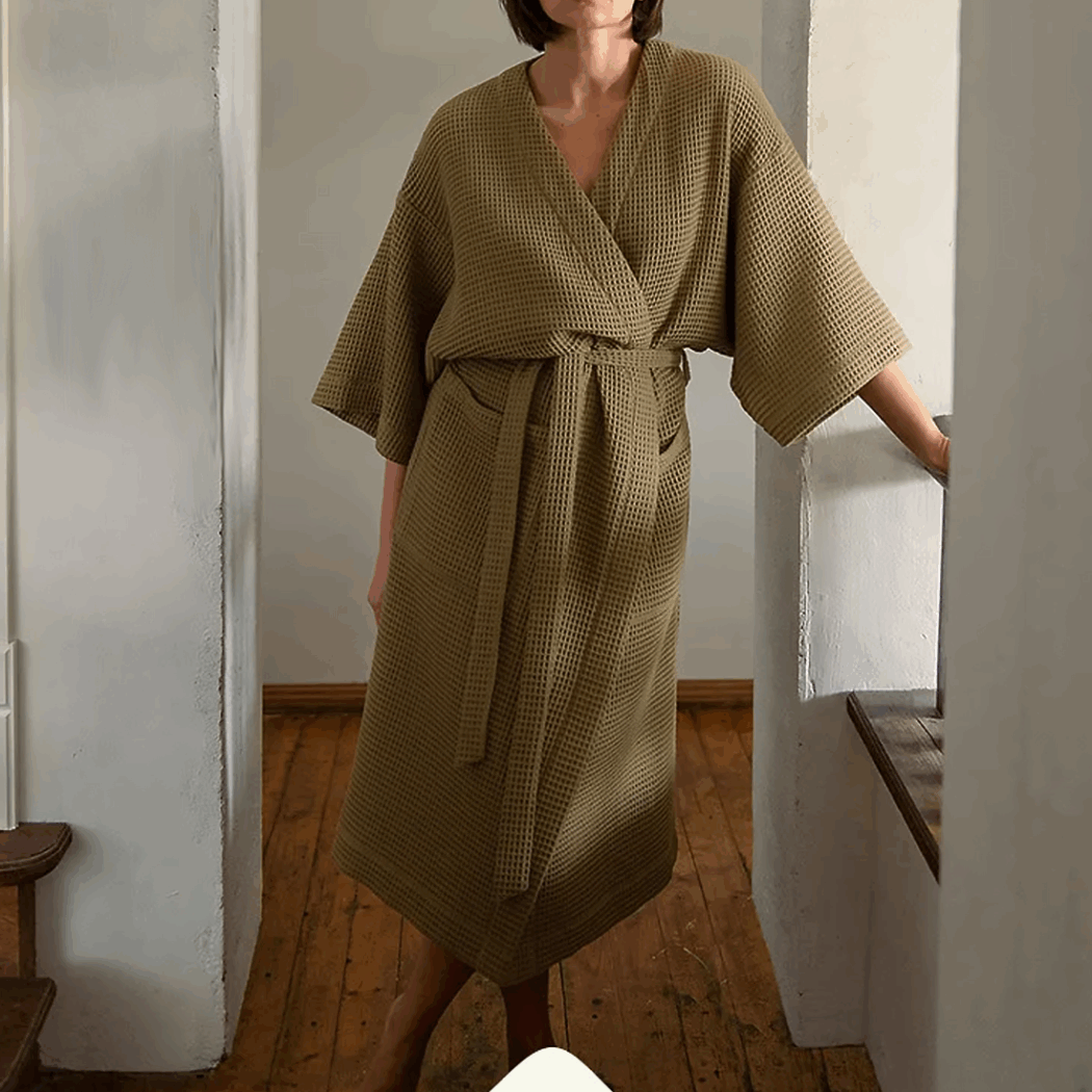 Photo d'une femme portant un peignoir en nid d'abeille de couleur vert olive, elle se tient debout dans un couloir